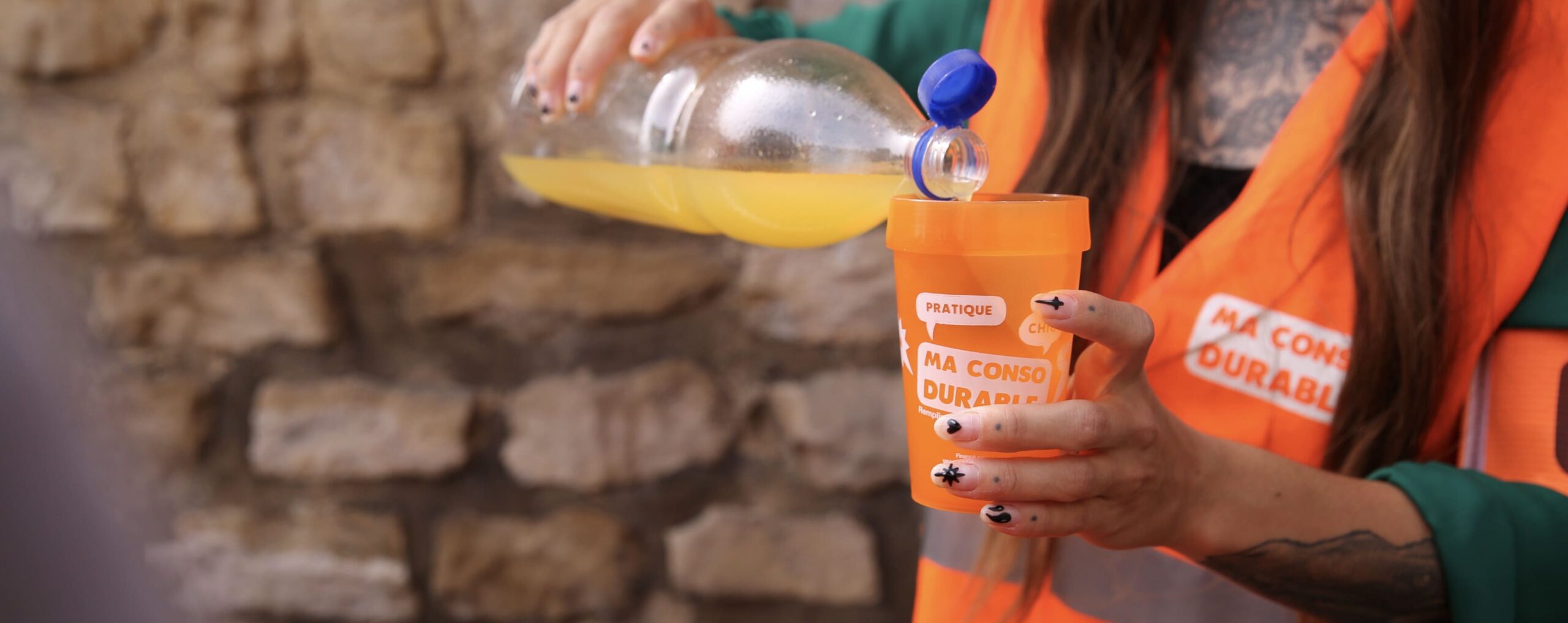 Bénévole en gilet orange versant une boisson dans un gobelet réutilisable Ma Conso Durable
