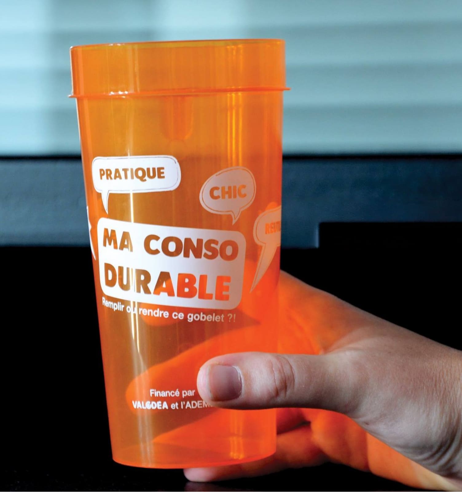 Main tenant un gobelet réutilisable orange Ma Conso Durable