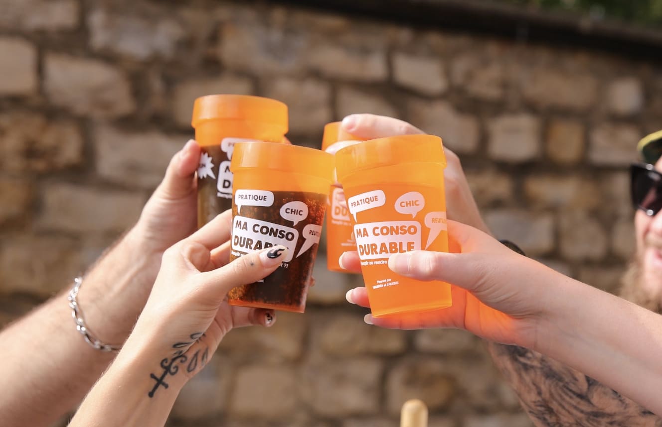 Trois personnes trinquent avec des gobelets réutilisables orange Ma Conso Durable
